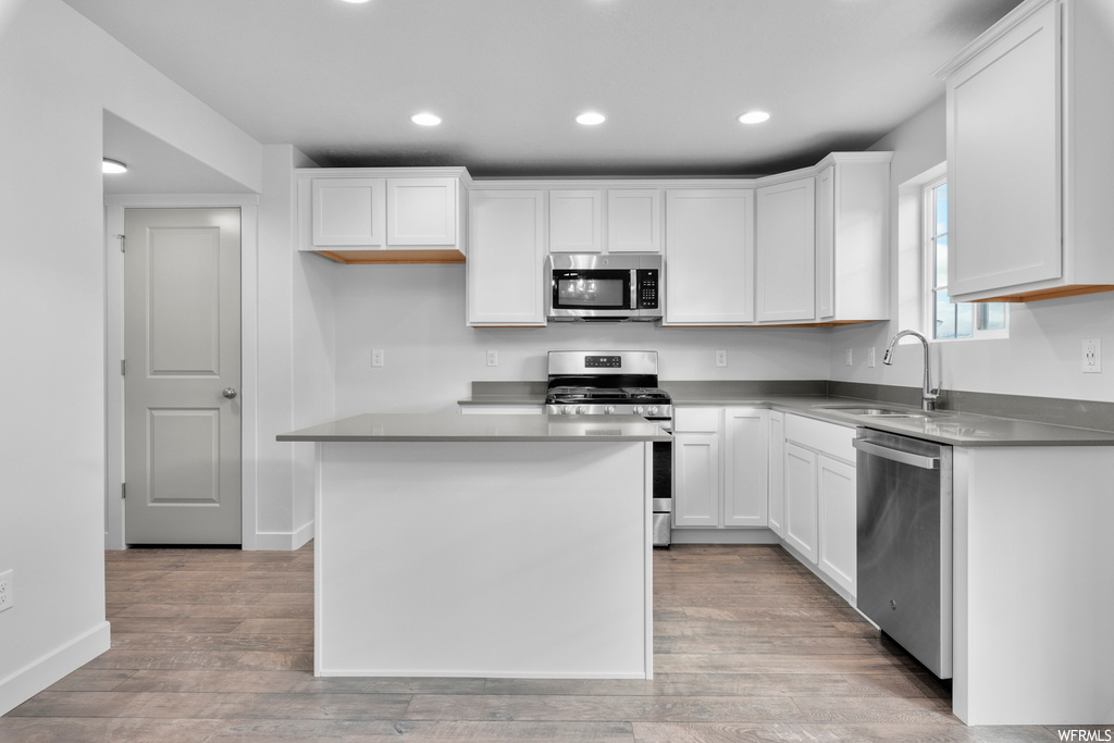 Kitchen featuring a center island, sink, light hardwood / wood-style flooring, appliances with stainless steel finishes, and white cabinetry