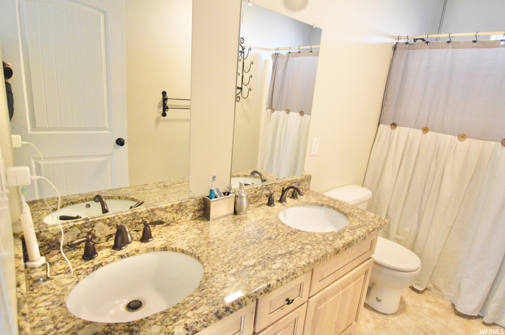 Bathroom featuring dual sinks, toilet, vanity with extensive cabinet space, and tile flooring