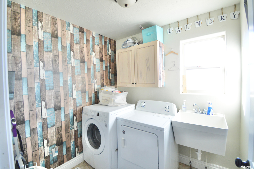 Washroom with cabinets, washing machine and clothes dryer, and sink