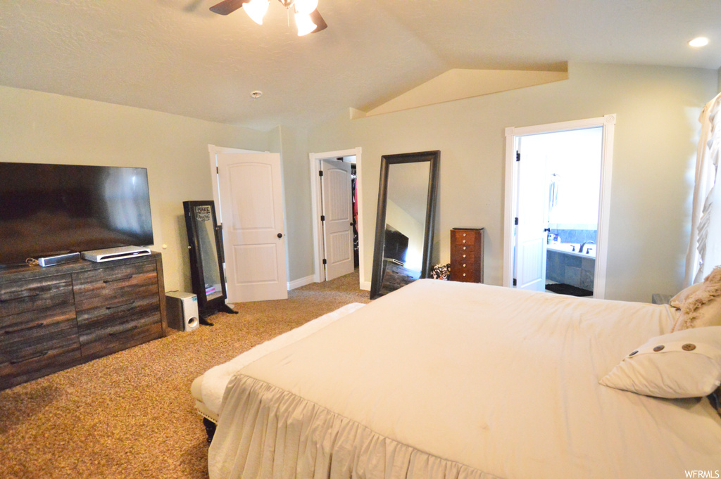 Carpeted bedroom featuring ensuite bathroom, ceiling fan, a walk in closet, and vaulted ceiling