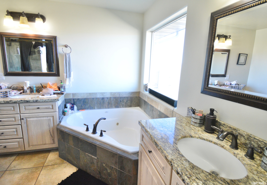 Bathroom with double vanity, tiled tub, and tile flooring