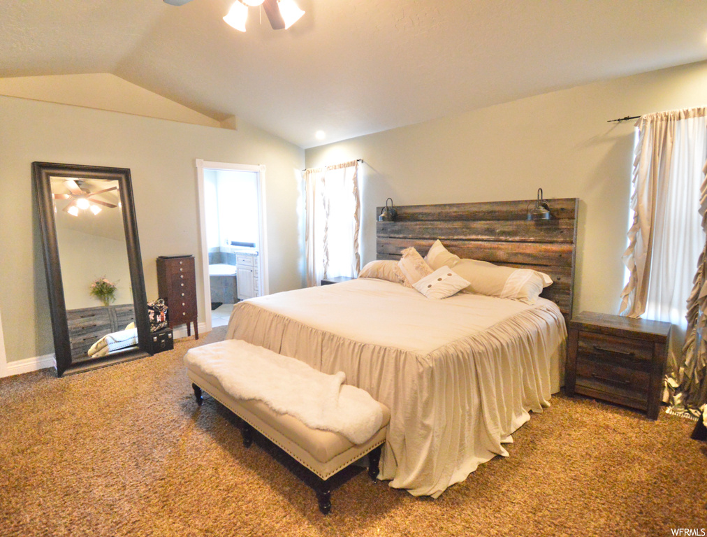 Carpeted bedroom with ceiling fan, connected bathroom, and vaulted ceiling