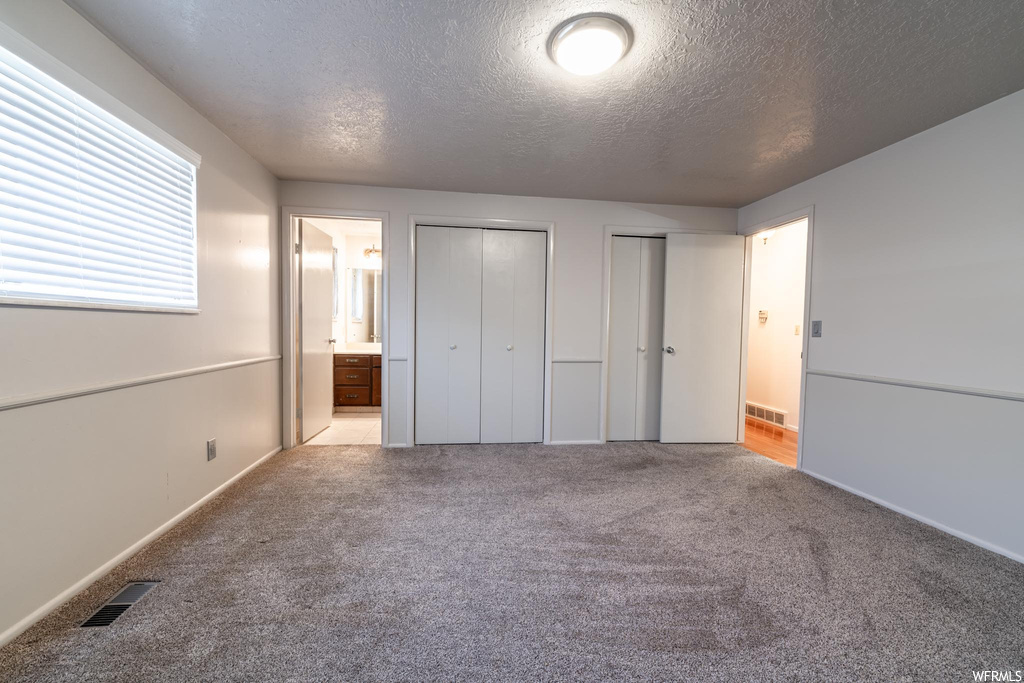 Unfurnished bedroom with connected bathroom, light carpet, a textured ceiling, and two closets