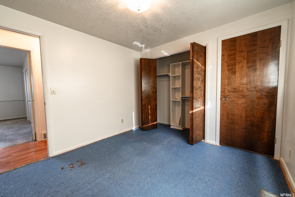 Unfurnished bedroom featuring dark carpet, a closet, and a textured ceiling