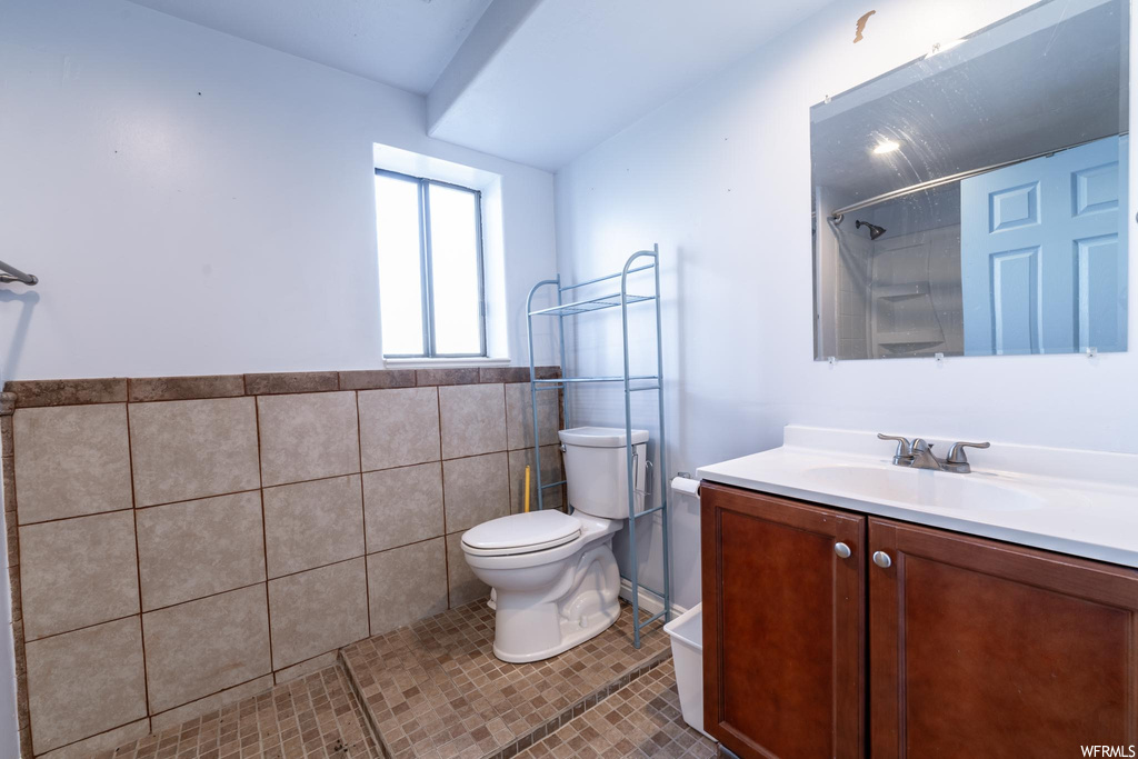 Bathroom with toilet, vanity with extensive cabinet space, tile walls, and tile flooring