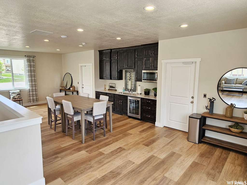 Kitchen with sink, a textured ceiling, light hardwood / wood-style flooring, and beverage cooler