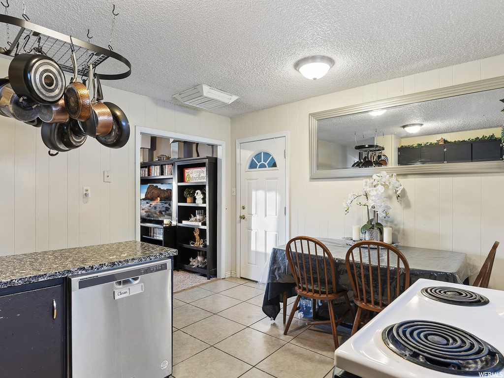 Kitchen featuring light tile floors, a textured ceiling, dishwasher, and stove