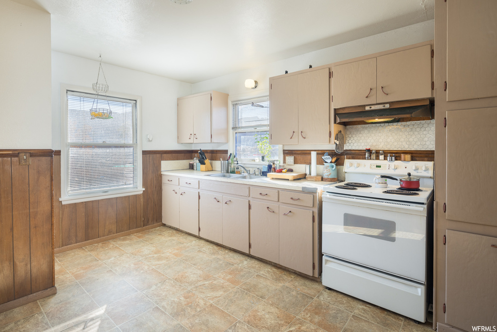 Kitchen with white electric range oven, hanging light fixtures, sink, tasteful backsplash, and light tile floors