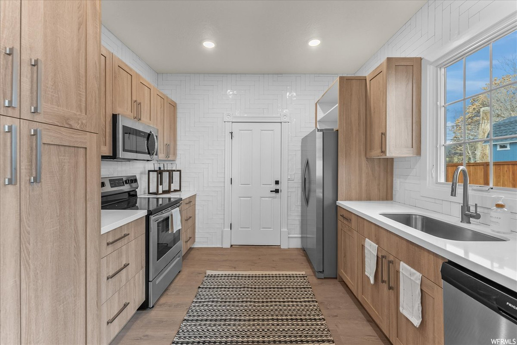 Kitchen with tasteful backsplash, sink, light hardwood / wood-style floors, and stainless steel appliances