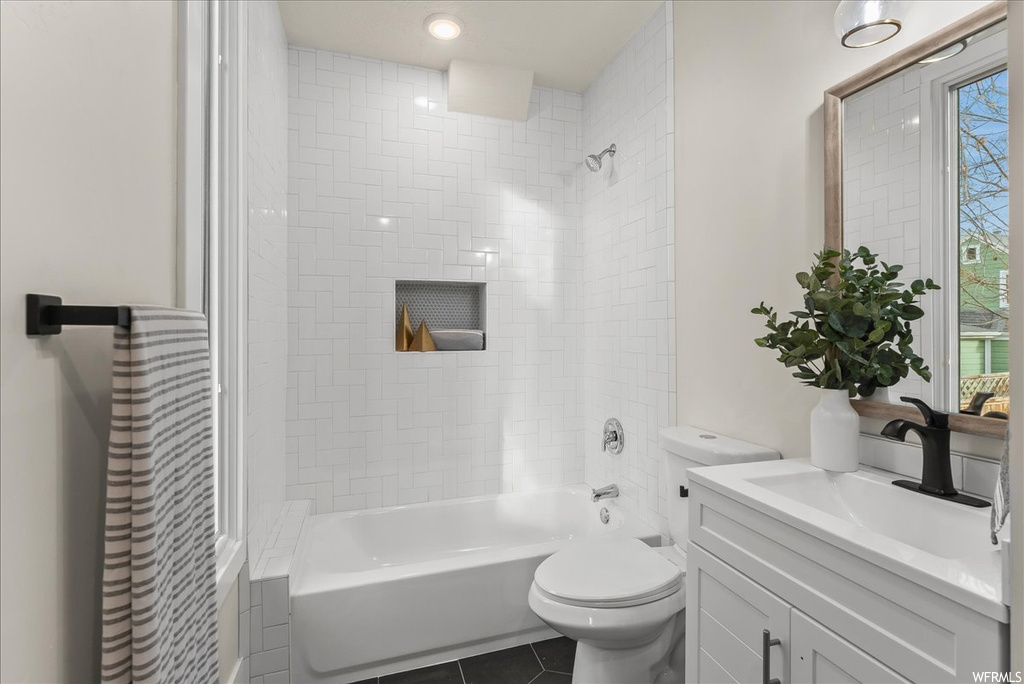 Full bathroom with toilet, tile floors, tiled shower / bath, and vanity with extensive cabinet space