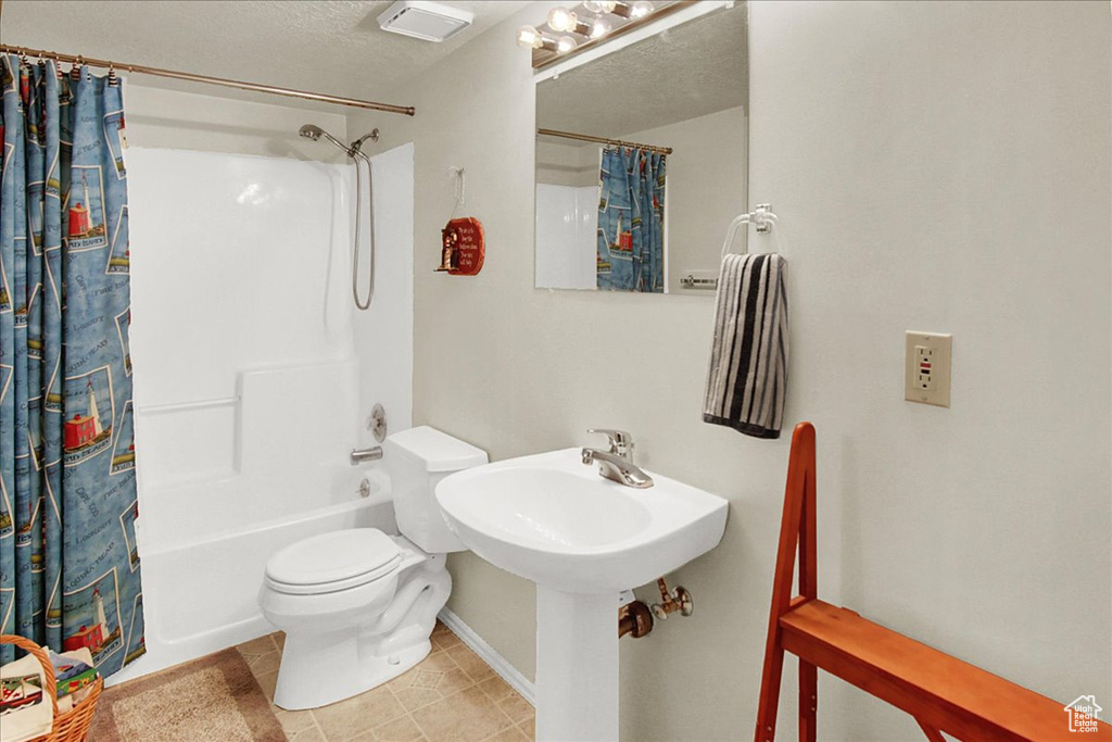 Bathroom featuring tile flooring, shower / tub combo, toilet, and a textured ceiling