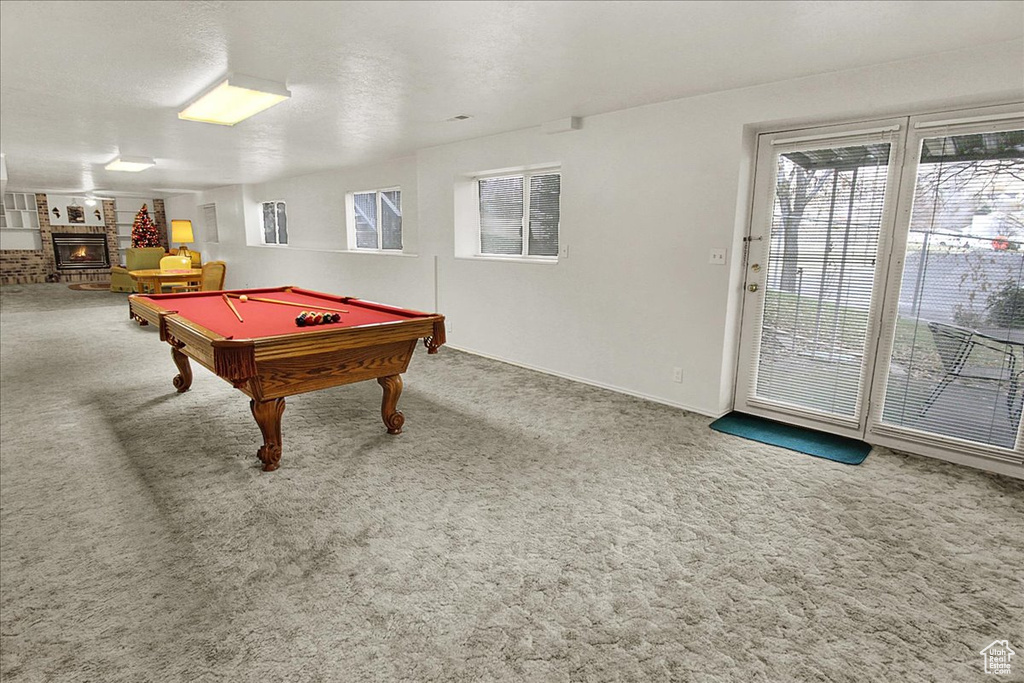 Game room featuring carpet, a fireplace, brick wall, pool table, and a textured ceiling