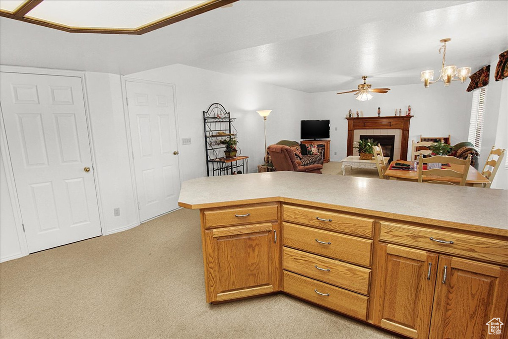 Kitchen with ceiling fan with notable chandelier, kitchen peninsula, pendant lighting, and light carpet