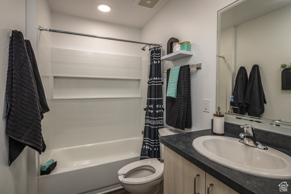 Full bathroom featuring large vanity, shower / bath combination with curtain, and toilet