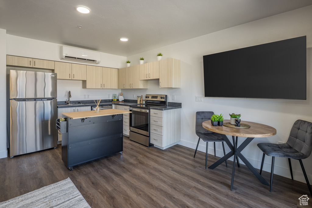 Kitchen featuring light brown cabinetry, a wall mounted AC, dark hardwood / wood-style flooring, stainless steel appliances, and an island with sink