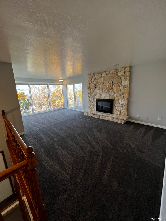 Unfurnished living room featuring a textured ceiling, a stone fireplace, and carpet flooring