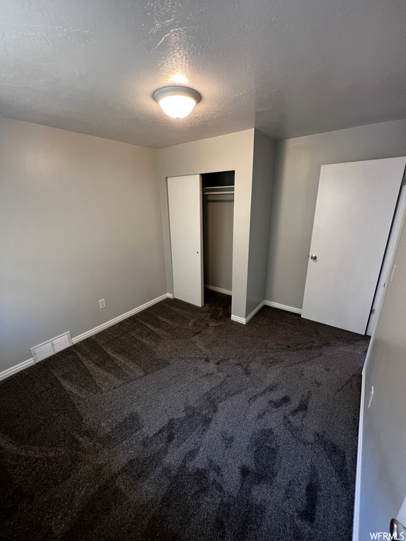 Unfurnished bedroom with dark carpet, a textured ceiling, and a closet