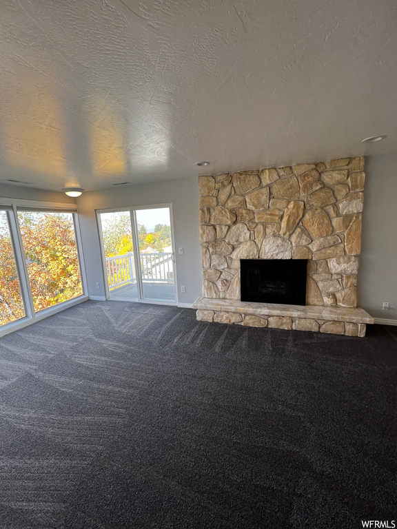 Unfurnished living room with a textured ceiling, a stone fireplace, and carpet flooring