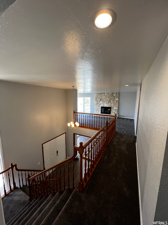 Stairway with a notable chandelier, a textured ceiling, a fireplace, and dark colored carpet