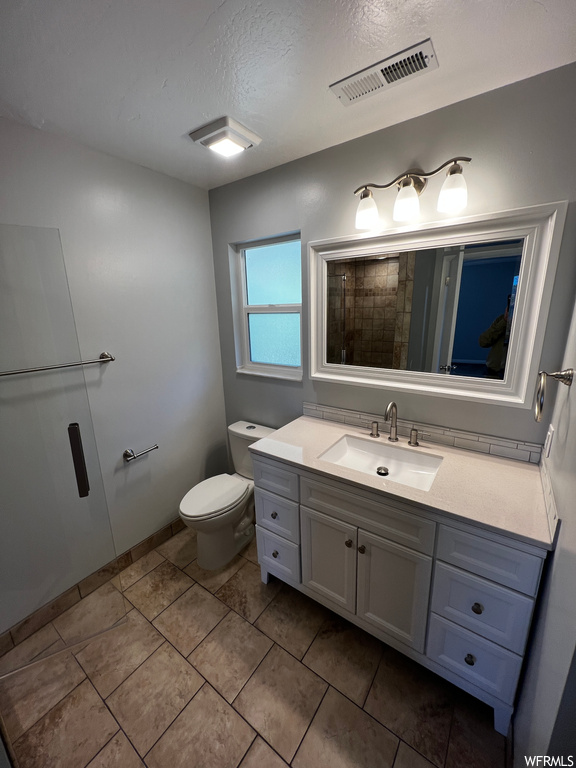 Bathroom with a textured ceiling, vanity, toilet, and tile floors