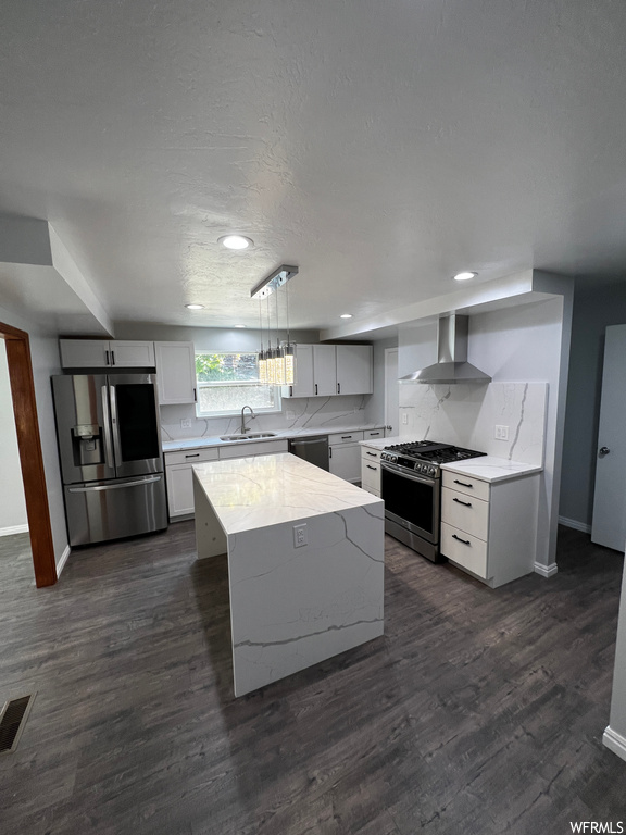 Kitchen featuring wall chimney range hood, stainless steel appliances, dark hardwood / wood-style floors, a kitchen island, and decorative light fixtures
