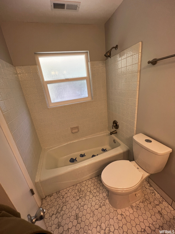 Bathroom featuring tiled shower / bath combo, toilet, and tile floors