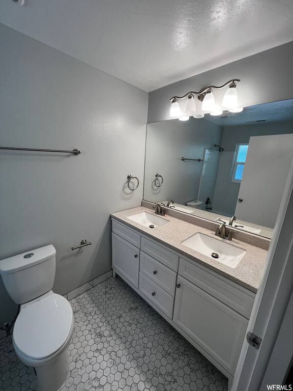 Bathroom featuring dual vanity, toilet, a textured ceiling, and tile floors