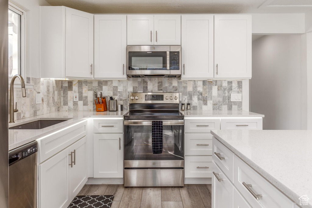 Kitchen featuring white cabinetry, sink, tasteful backsplash, appliances with stainless steel finishes, and light hardwood / wood-style flooring