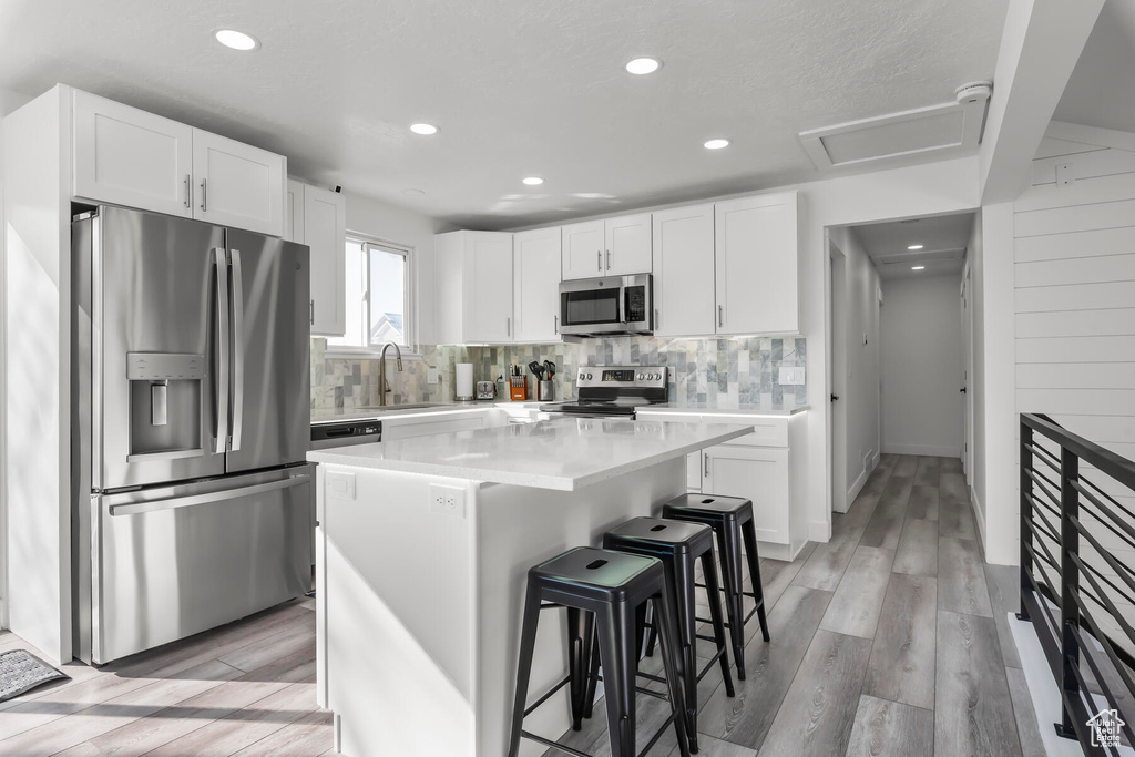Kitchen featuring a kitchen island, appliances with stainless steel finishes, light hardwood / wood-style flooring, a breakfast bar, and white cabinetry
