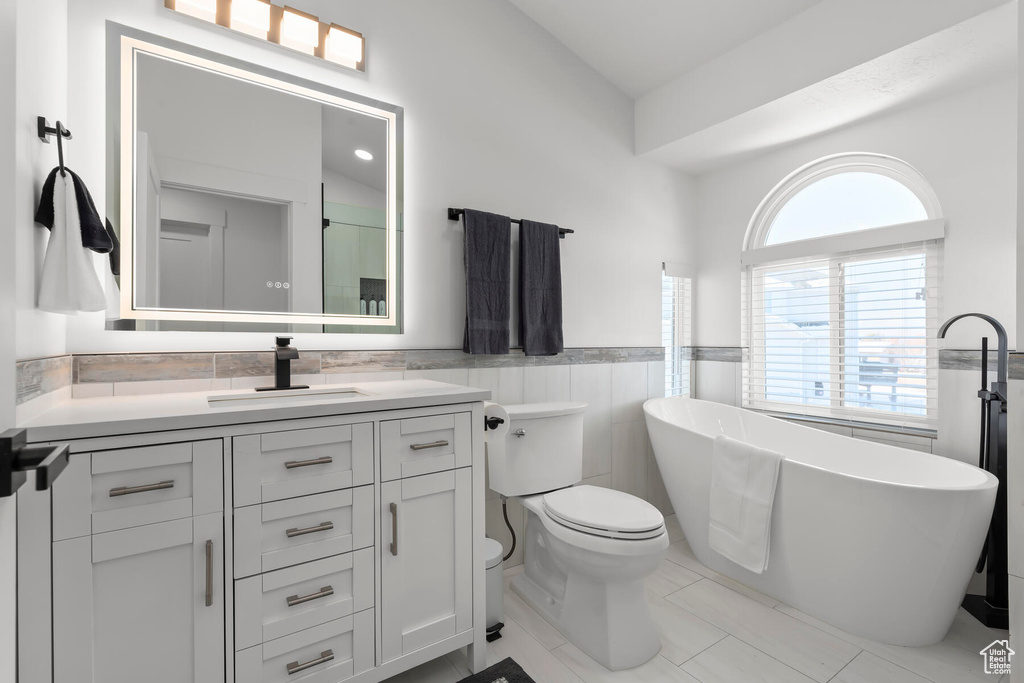Bathroom featuring a bathtub, tile walls, toilet, tile floors, and oversized vanity