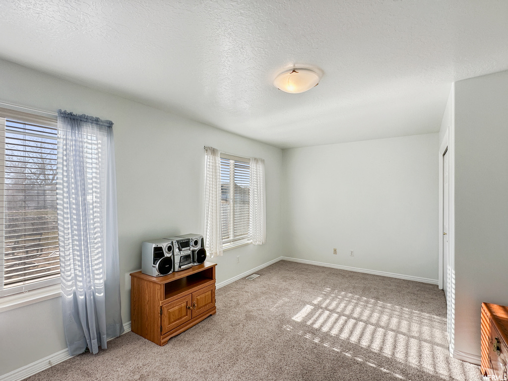 Empty room with light colored carpet and a textured ceiling