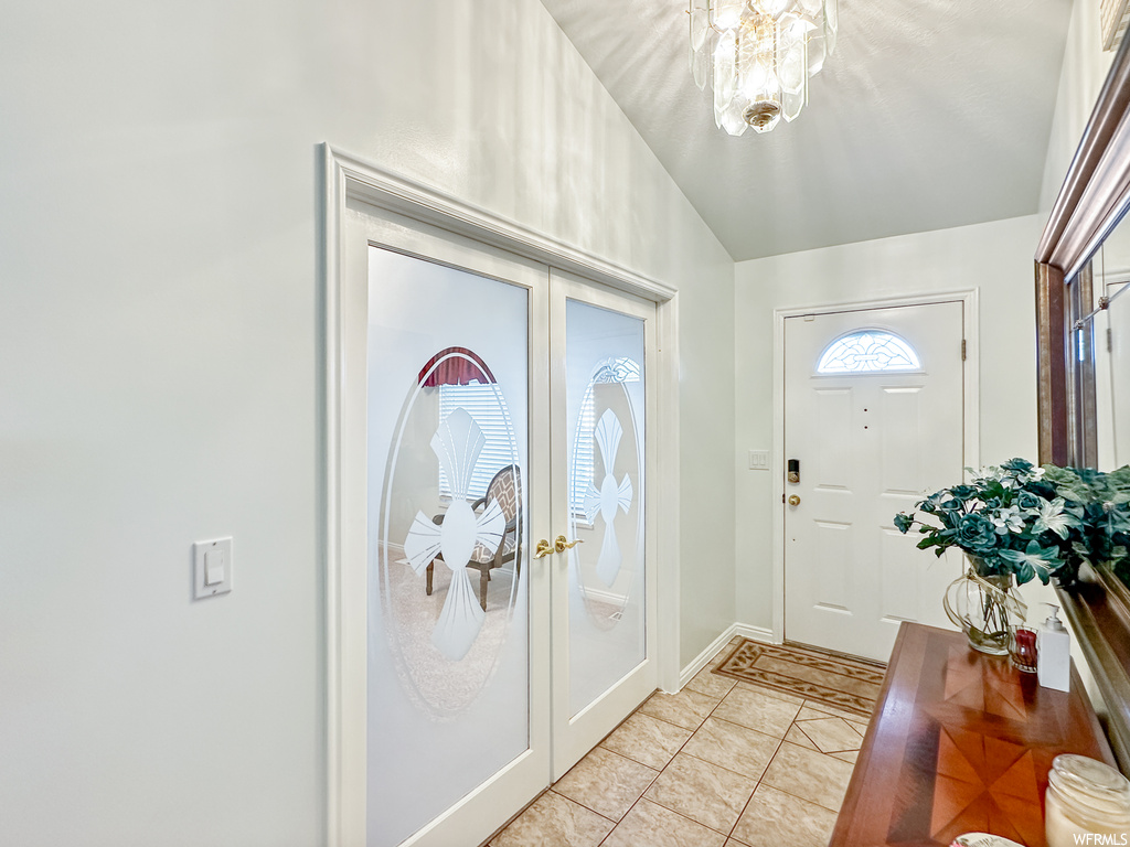 Tiled entrance foyer with french doors, an inviting chandelier, and vaulted ceiling