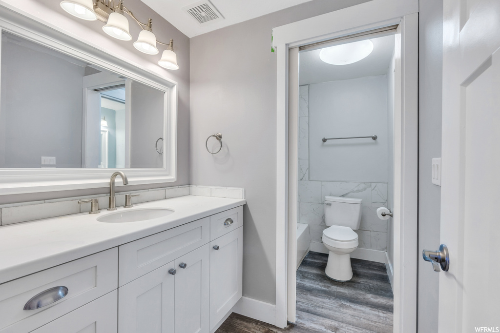 Bathroom with toilet, hardwood / wood-style floors, tile walls, and vanity