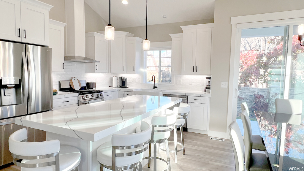 Kitchen featuring pendant lighting, white cabinets, and wall chimney range hood