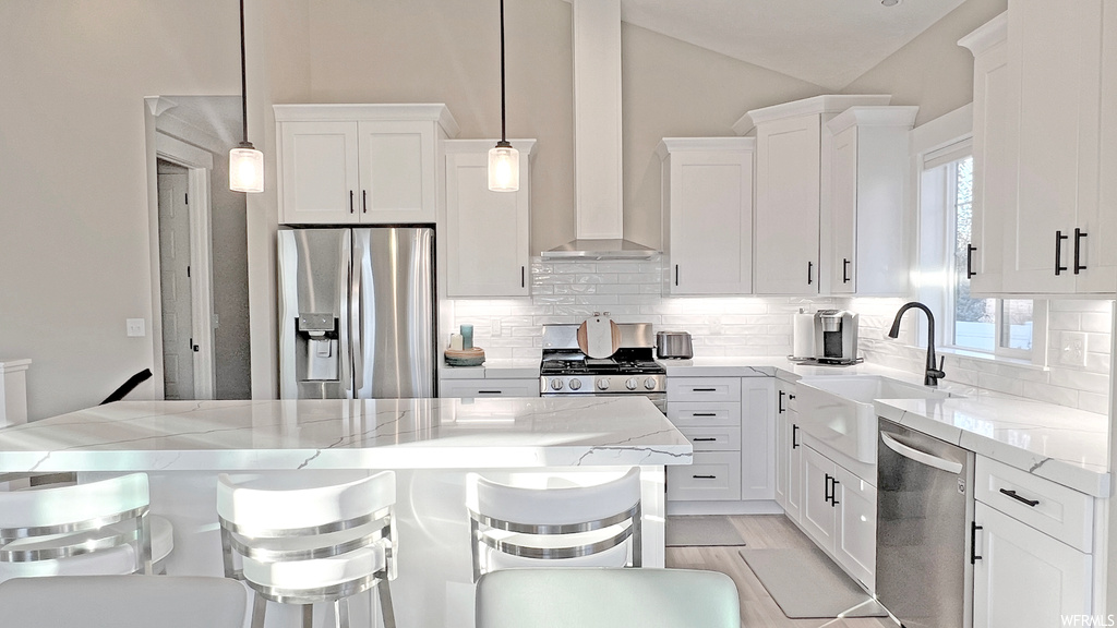 Kitchen with hanging light fixtures, white cabinets, light stone countertops, and appliances with stainless steel finishes