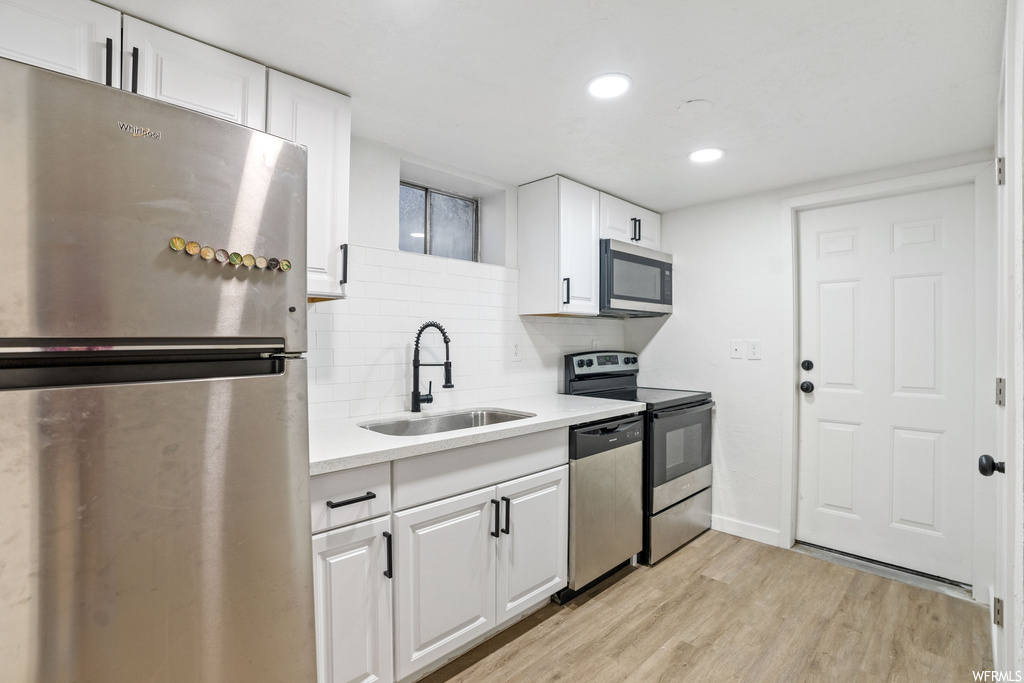 Kitchen featuring sink, light hardwood / wood-style flooring, stainless steel appliances, white cabinets, and tasteful backsplash