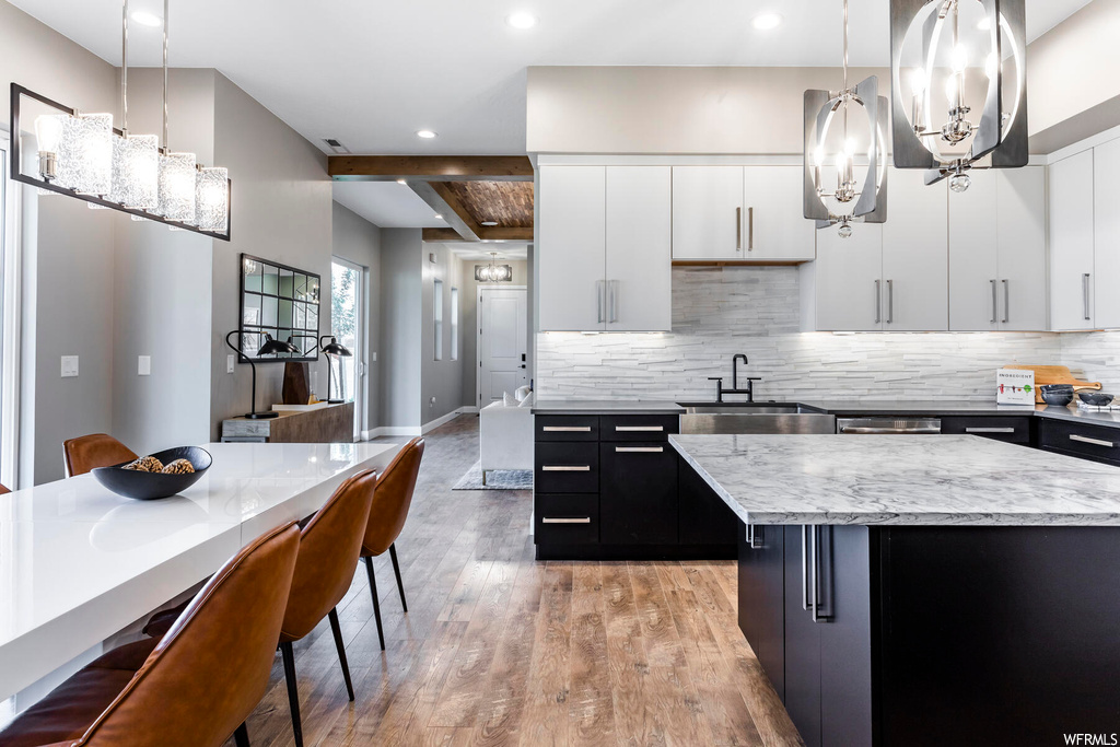 Kitchen featuring backsplash, hanging light fixtures, white cabinets, and light hardwood / wood-style floors