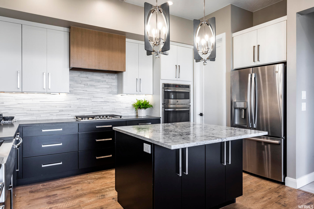 Kitchen with a center island, hanging light fixtures, appliances with stainless steel finishes, and white cabinetry