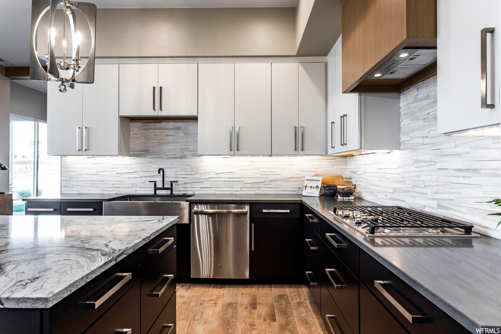 Kitchen featuring appliances with stainless steel finishes, wall chimney range hood, white cabinets, backsplash, and light hardwood / wood-style flooring