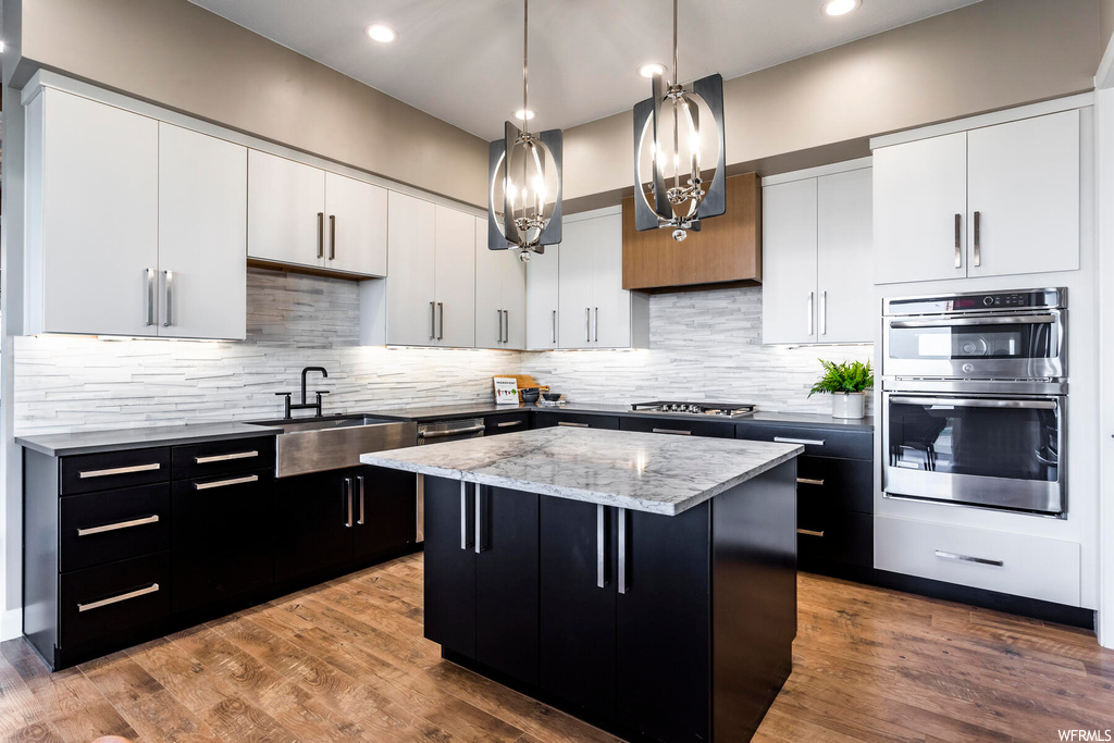 Kitchen featuring sink, tasteful backsplash, double oven, light hardwood / wood-style flooring, and a kitchen island