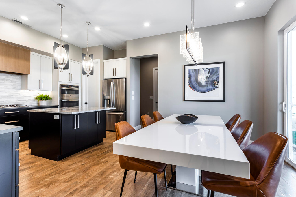 Interior space featuring appliances with stainless steel finishes, pendant lighting, a center island, backsplash, and white cabinetry