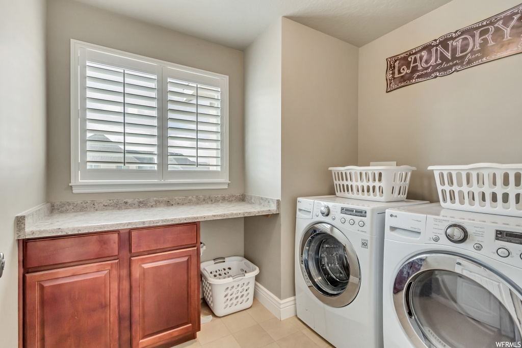 Clothes washing area with cabinets, light tile flooring, and separate washer and dryer