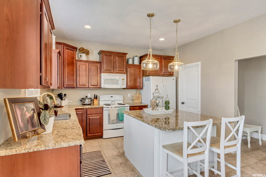 Kitchen with light stone counters, white appliances, a breakfast bar, and pendant lighting