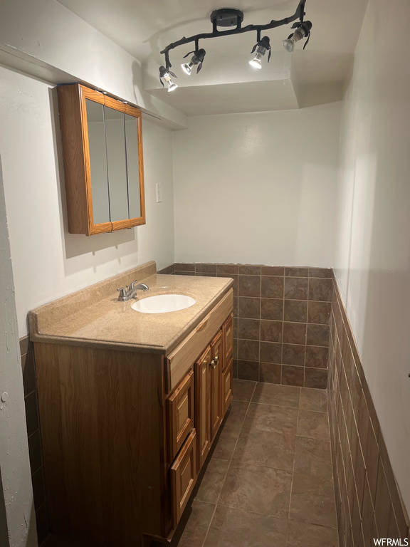 Bathroom featuring tile flooring, rail lighting, tile walls, and vanity