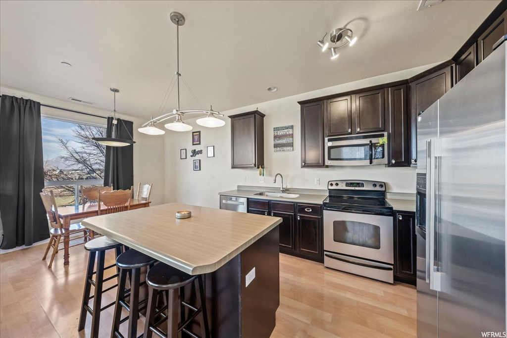 Kitchen featuring a center island, stainless steel appliances, light wood-type flooring, decorative light fixtures, and dark brown cabinetry