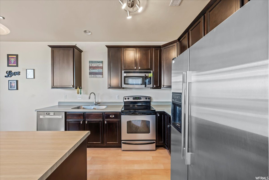 Kitchen featuring dark brown cabinets, sink, light hardwood / wood-style flooring, and stainless steel appliances