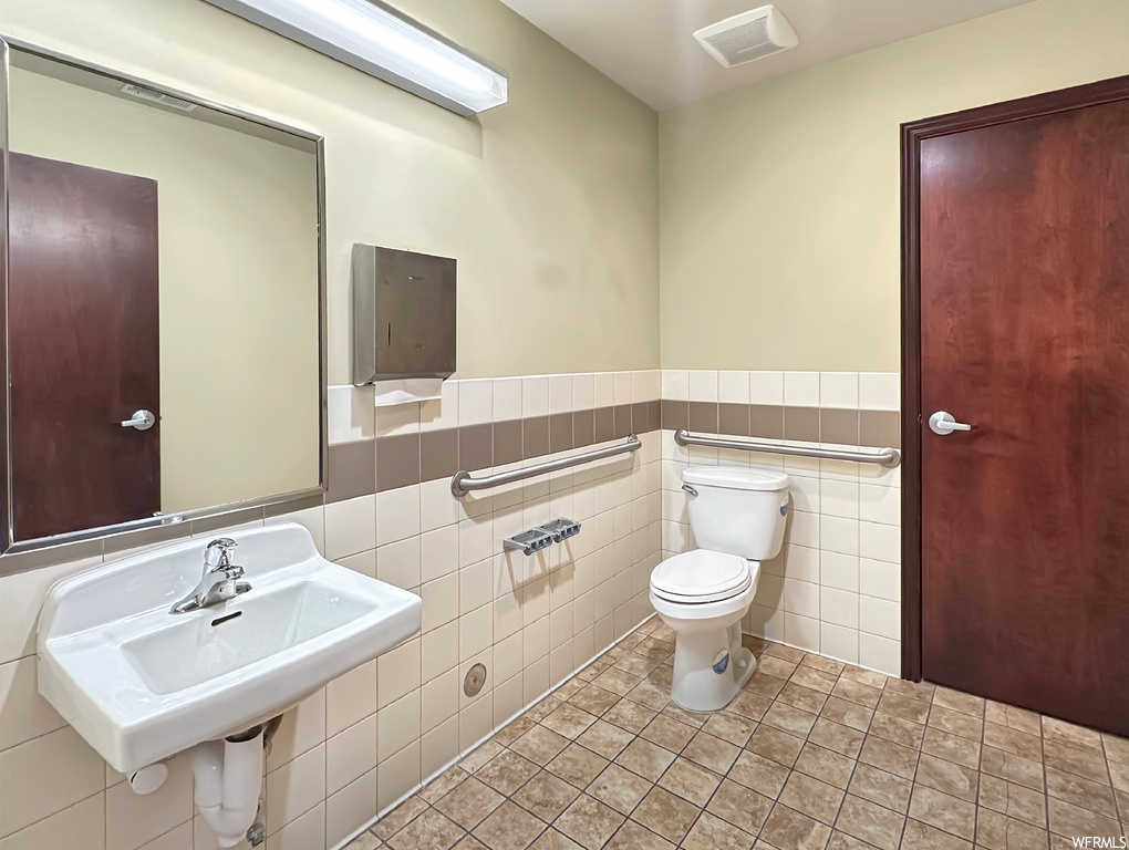 Bathroom featuring toilet, tile floors, sink, and tile walls