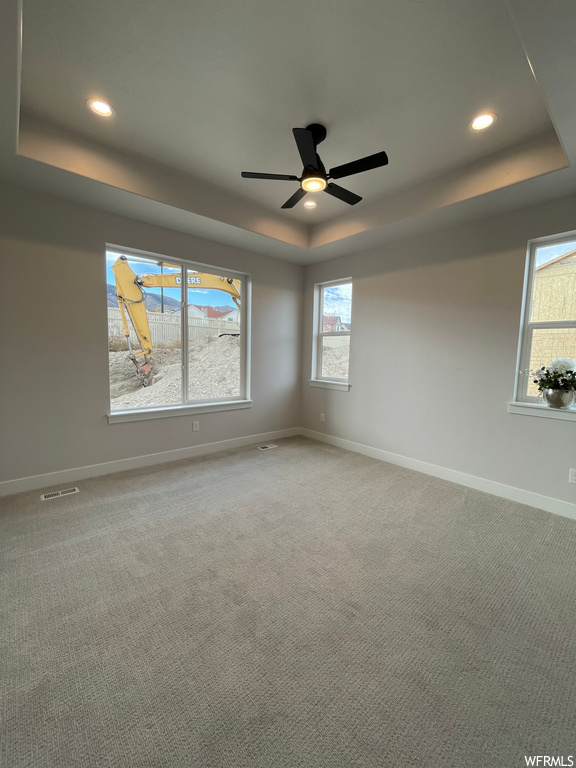 Unfurnished room featuring a raised ceiling, light carpet, and ceiling fan