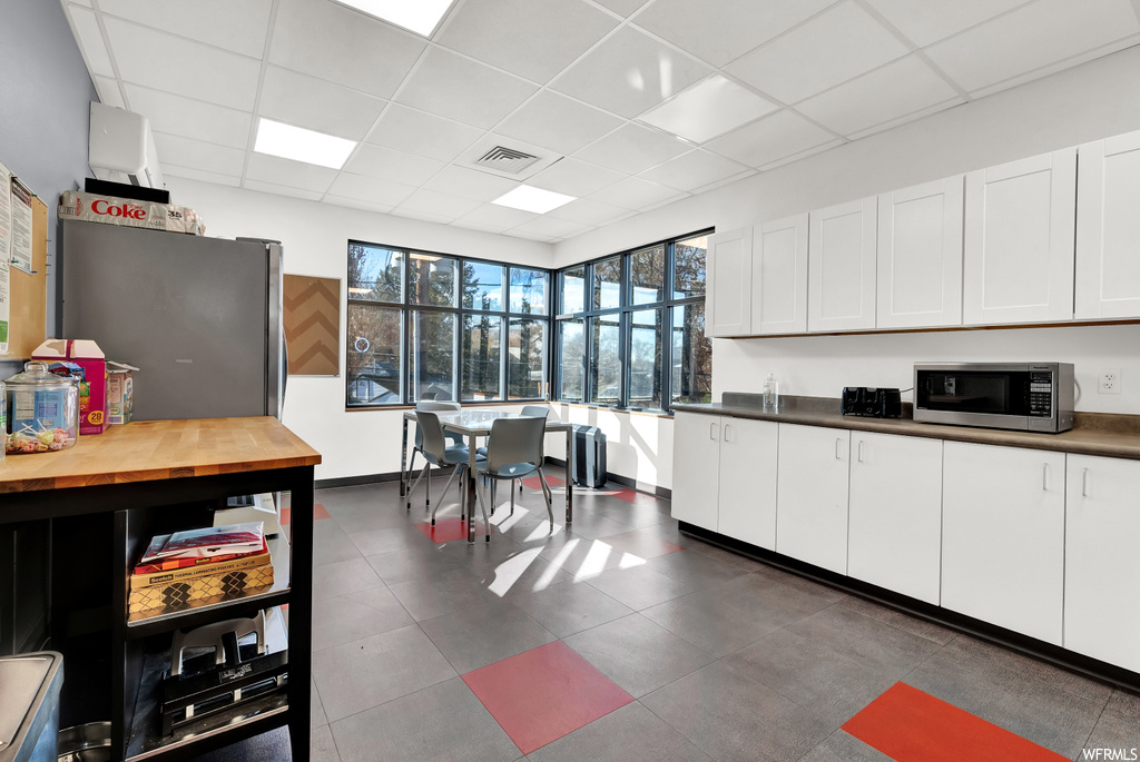 Kitchen featuring a paneled ceiling, dark tile flooring, white cabinets, and appliances with stainless steel finishes