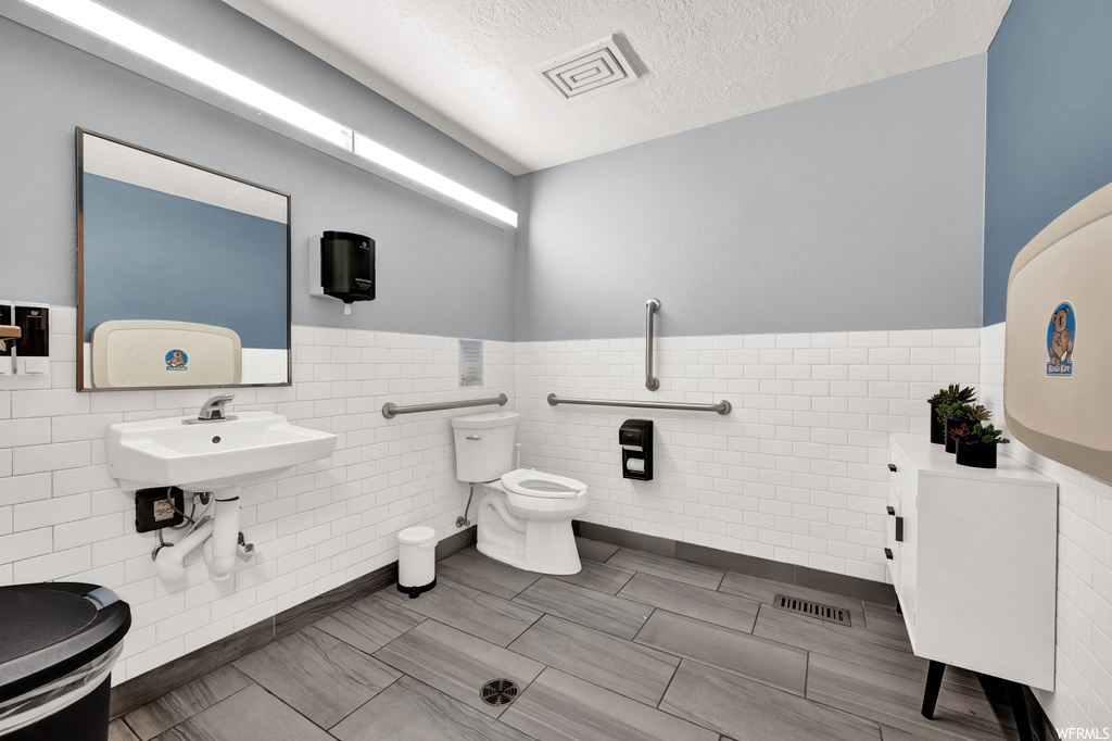 Bathroom featuring toilet, sink, tile walls, and tile flooring